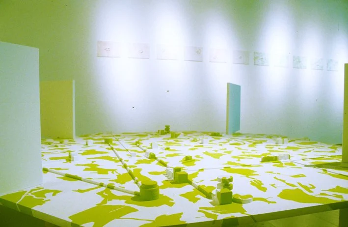 Modèles architecturaux en jaune et blanc sur une surface, avec structures cylindriques et parois dans une pièce lumineuse.