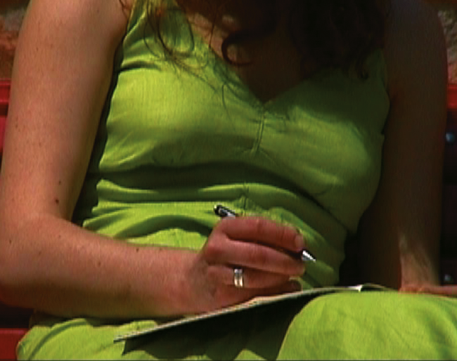 Une femme en robe verte écrit dans un carnet pendant qu'elle est assise.