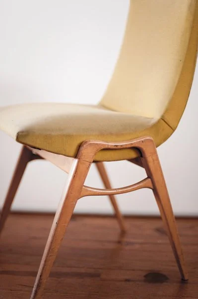 Chaise ancienne en bois avec assise et dossier en tissu beige, pied en bois clair sur un sol en bois.