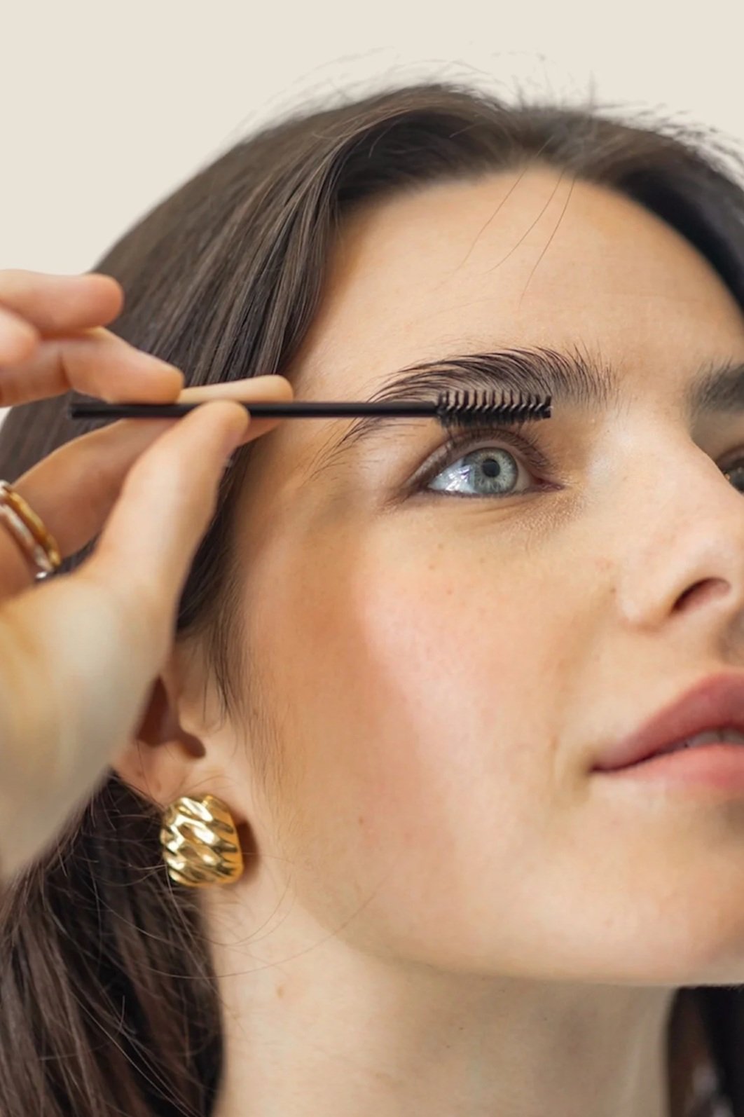 A woman with blue eyes getting her eyelashes brushed by a stylist.