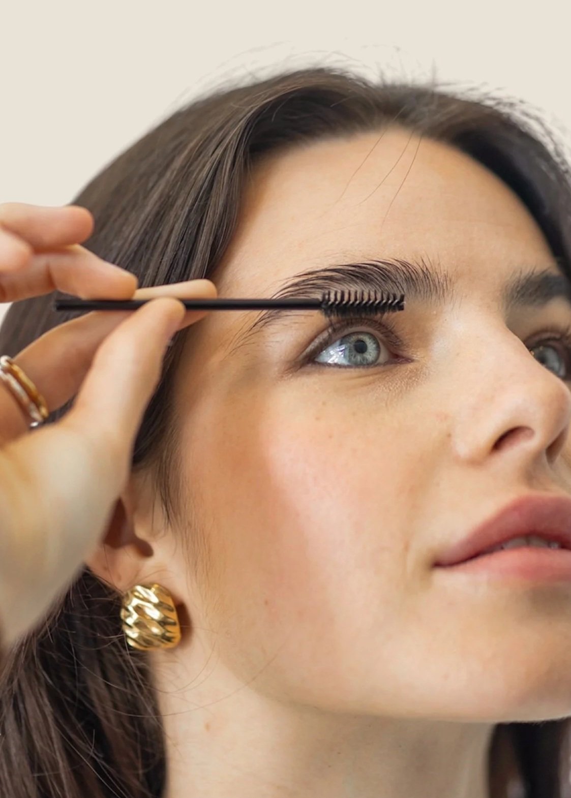 Close-up of a woman with blue eyes having her eyelashes brushed with a mascara wand by a makeup artist.