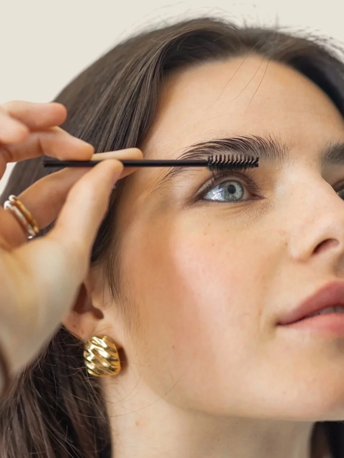 Close-up of a woman with blue eyes getting her eyelashes styled with a brush