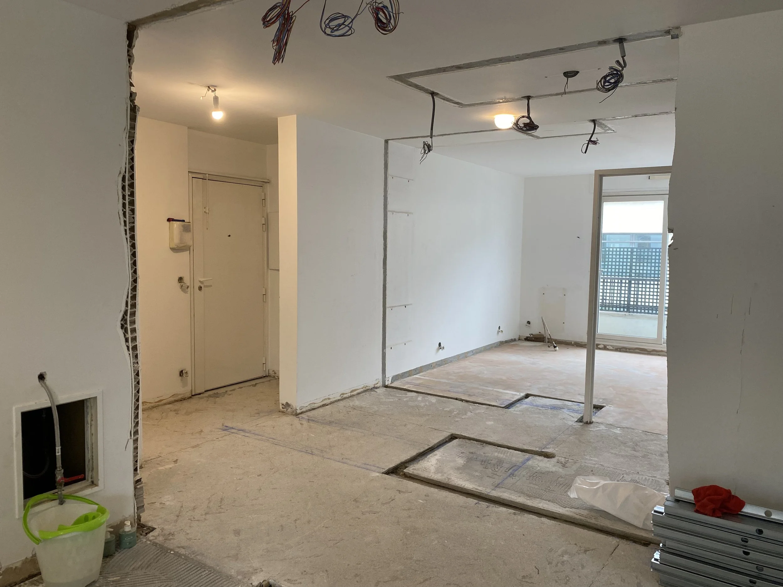 Interior of a room under construction or renovation with exposed wiring, unfinished walls, and construction materials on the floor.