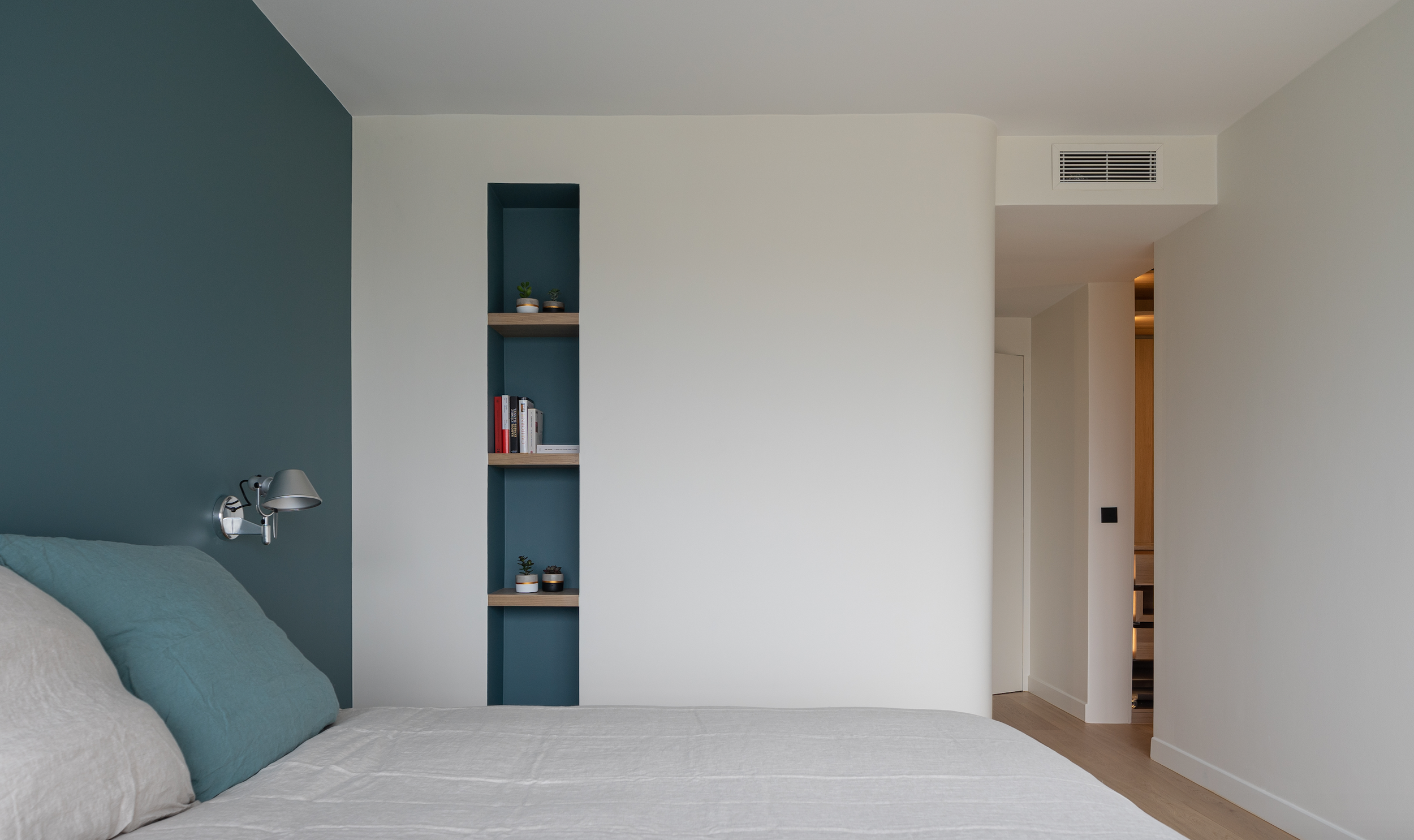 Modern bedroom with teal accent wall, nightstand, and built-in bookshelf with plants and books