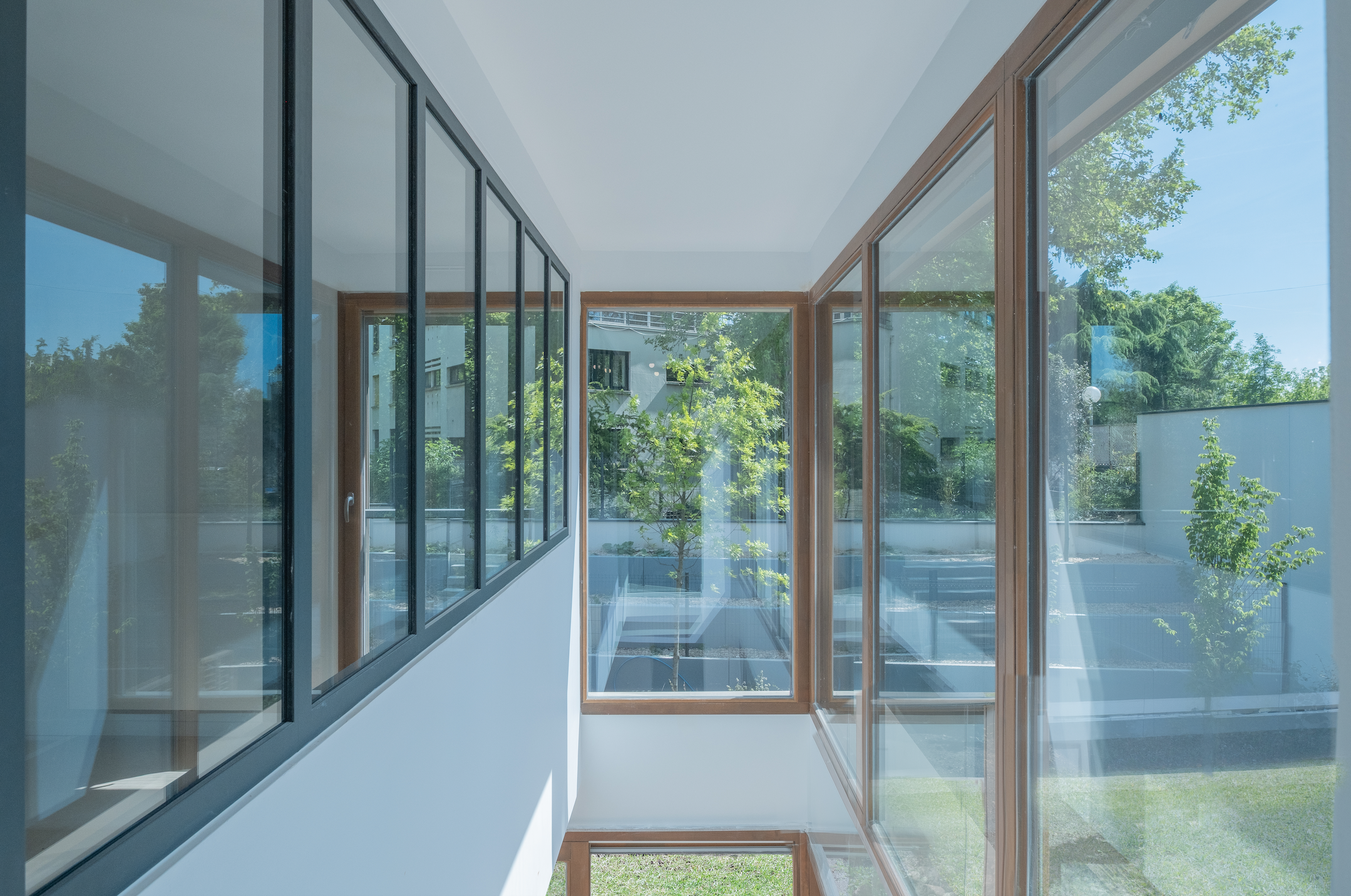 Interior view of modern building with large glass windows showing green trees and blue sky outside.