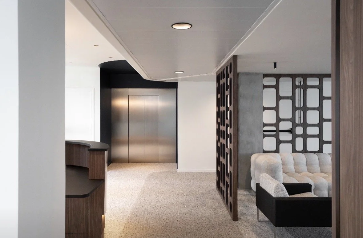 Modern office lobby with elevator and seating area separated by decorative wooden partition.