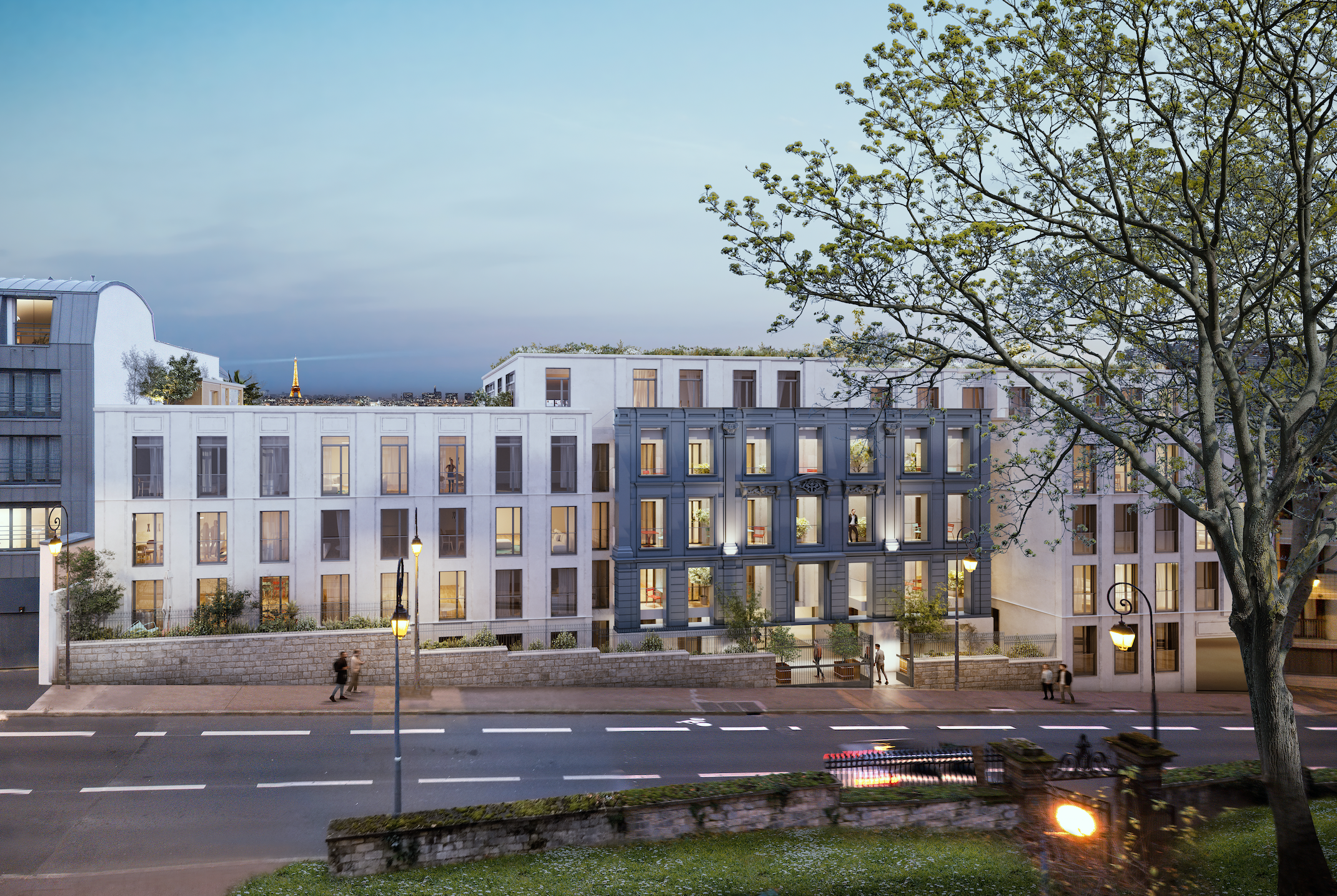 Modern white and gray apartment buildings with large windows along a street, some with lights on, in the evening. The scene includes street lamps, a stone wall, trees, and pedestrians.