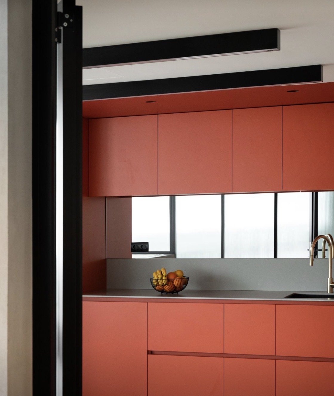 Modern kitchen with pink cabinets, a bowl of fruits, and a window with a city view.