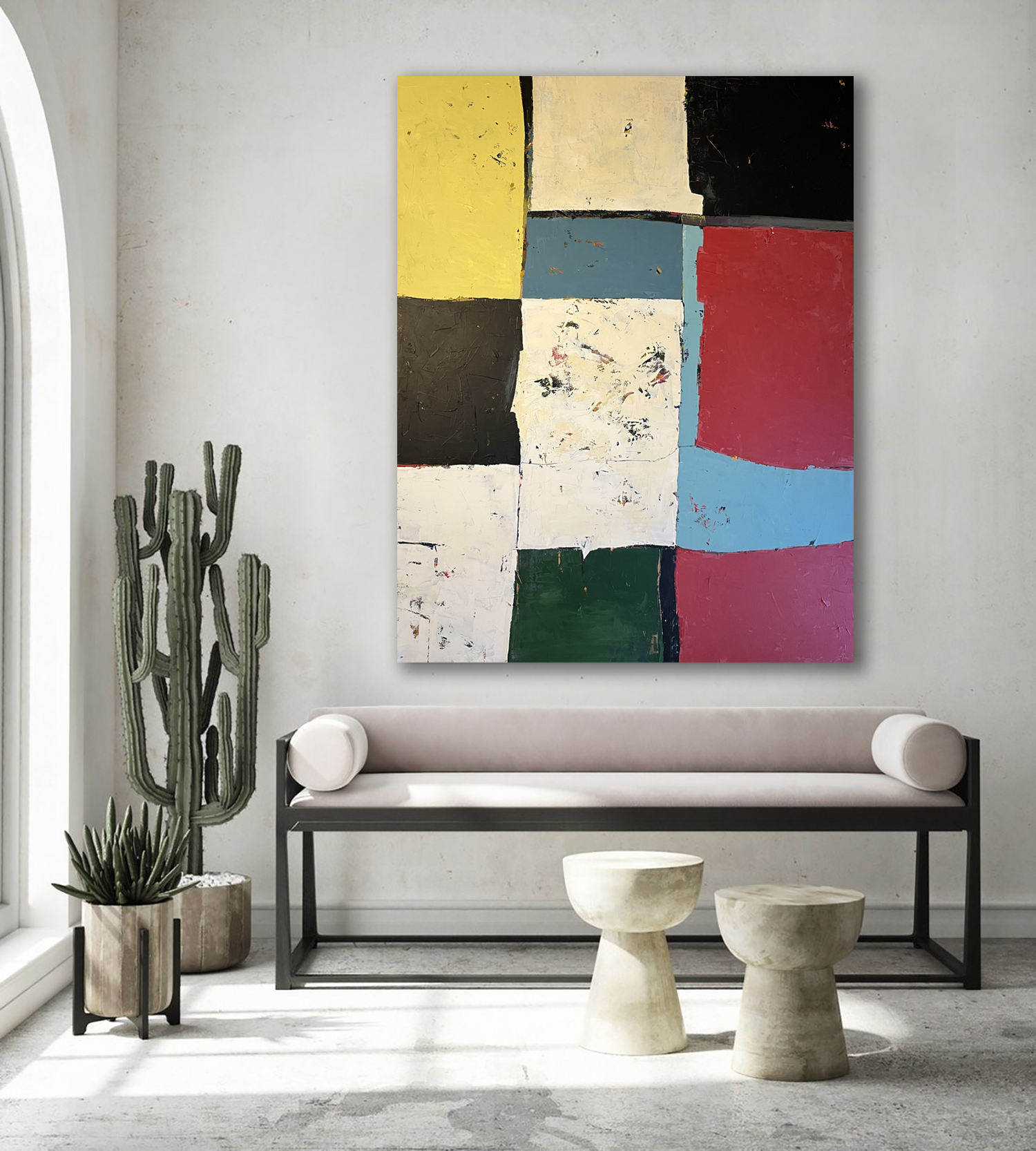 Modern living room with a large abstract painting on the wall, a white cushioned bench with circular pillows, two small round stone tables, and a tall potted cactus plant near the window.