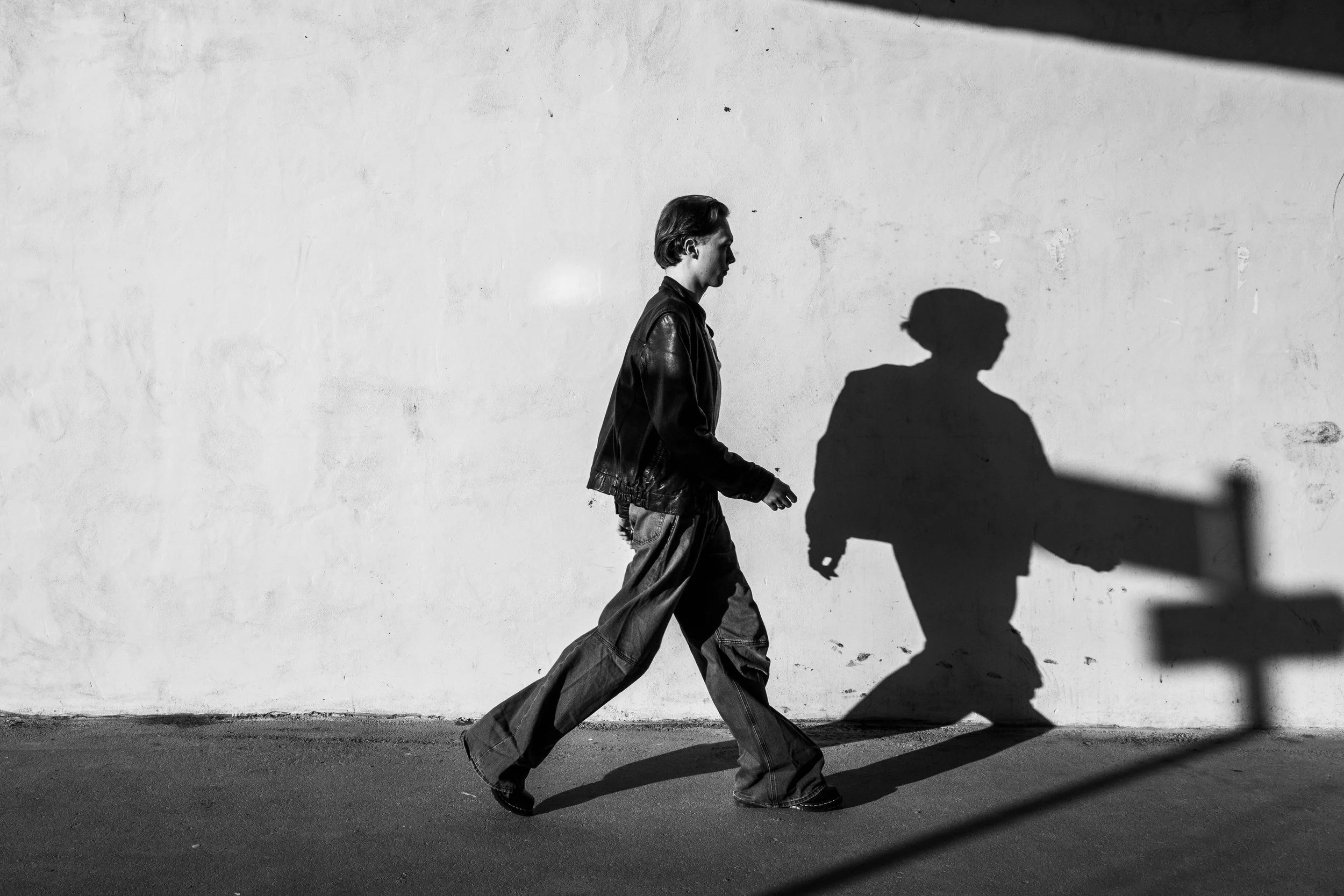 A person walking along a street casts a shadows on a blank wall, with sunlight creating a dark silhouette of the person's head and shoulders.