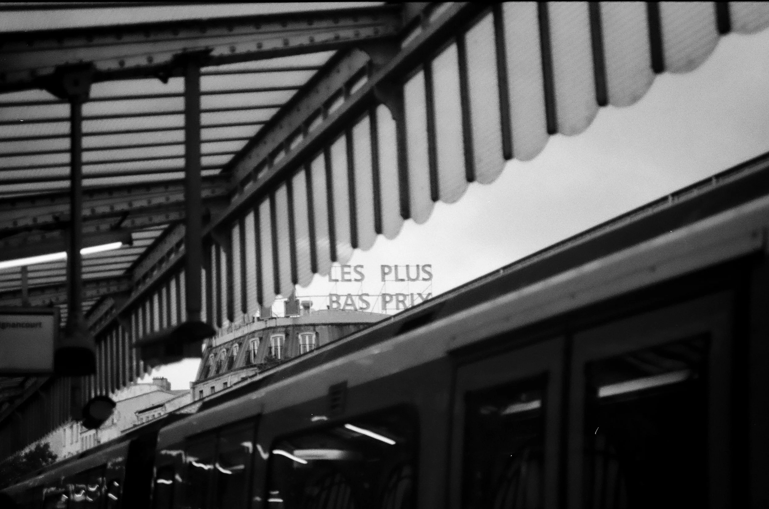 Black and white photo showing the exterior of a building with a decorative balcony and a sign that reads "LES PLUS".