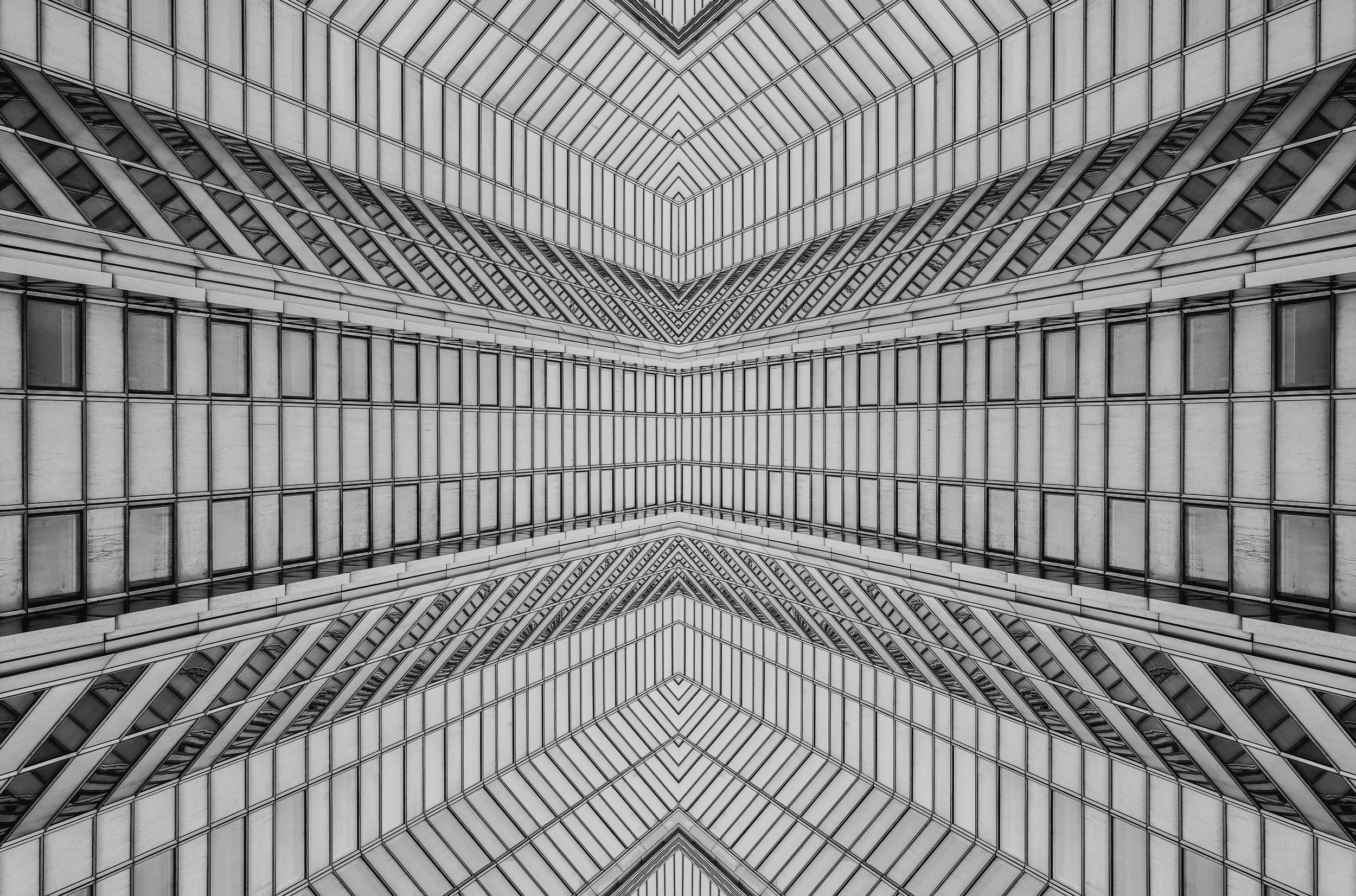 The photo shows the interior of a modern building with high ceilings and symmetrical architecture, featuring a pattern of glass and steel elements forming an intricate geometric design.