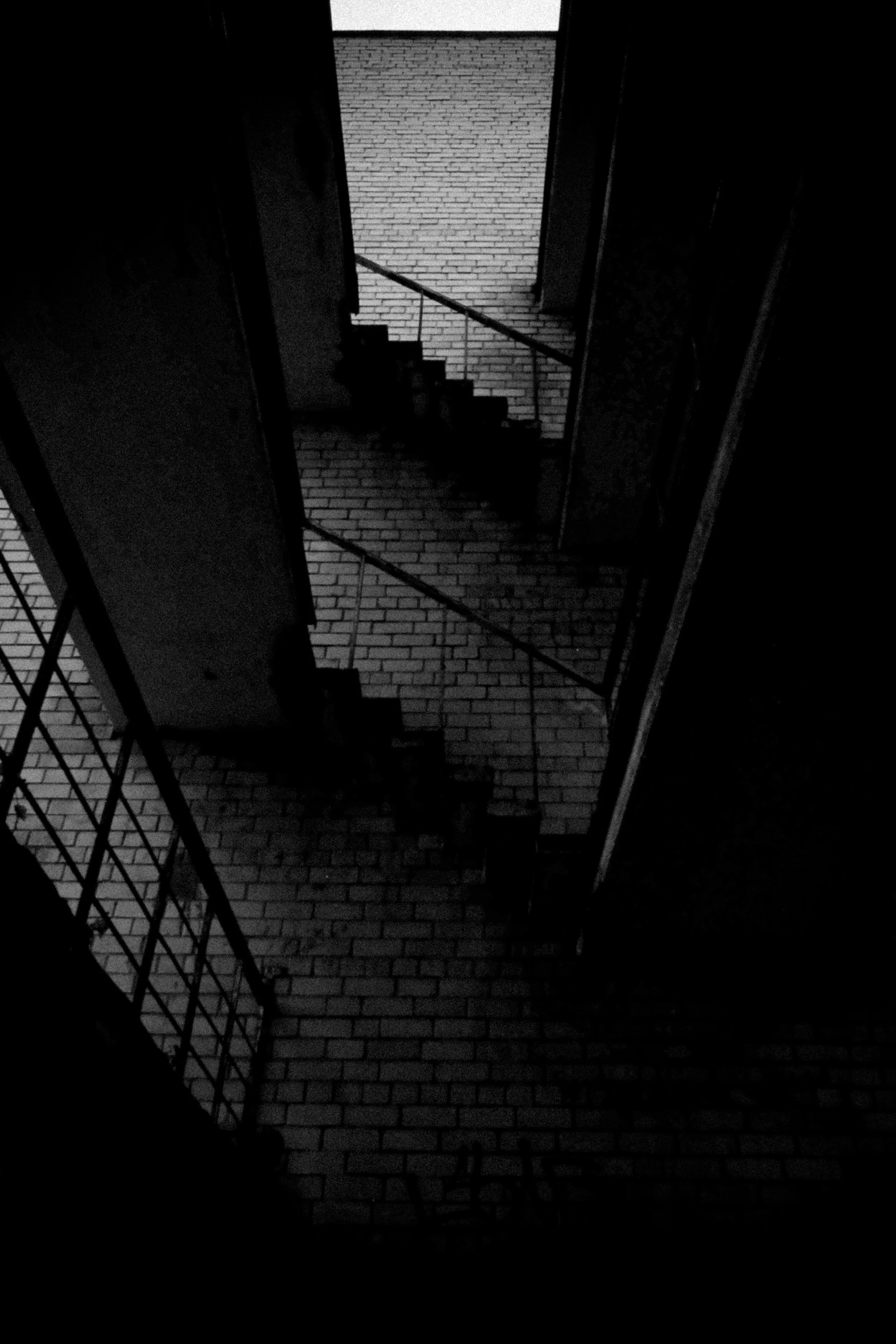 Dark staircase leading to a brick wall in a narrow, dimly lit corridor, with metal railings on the sides.