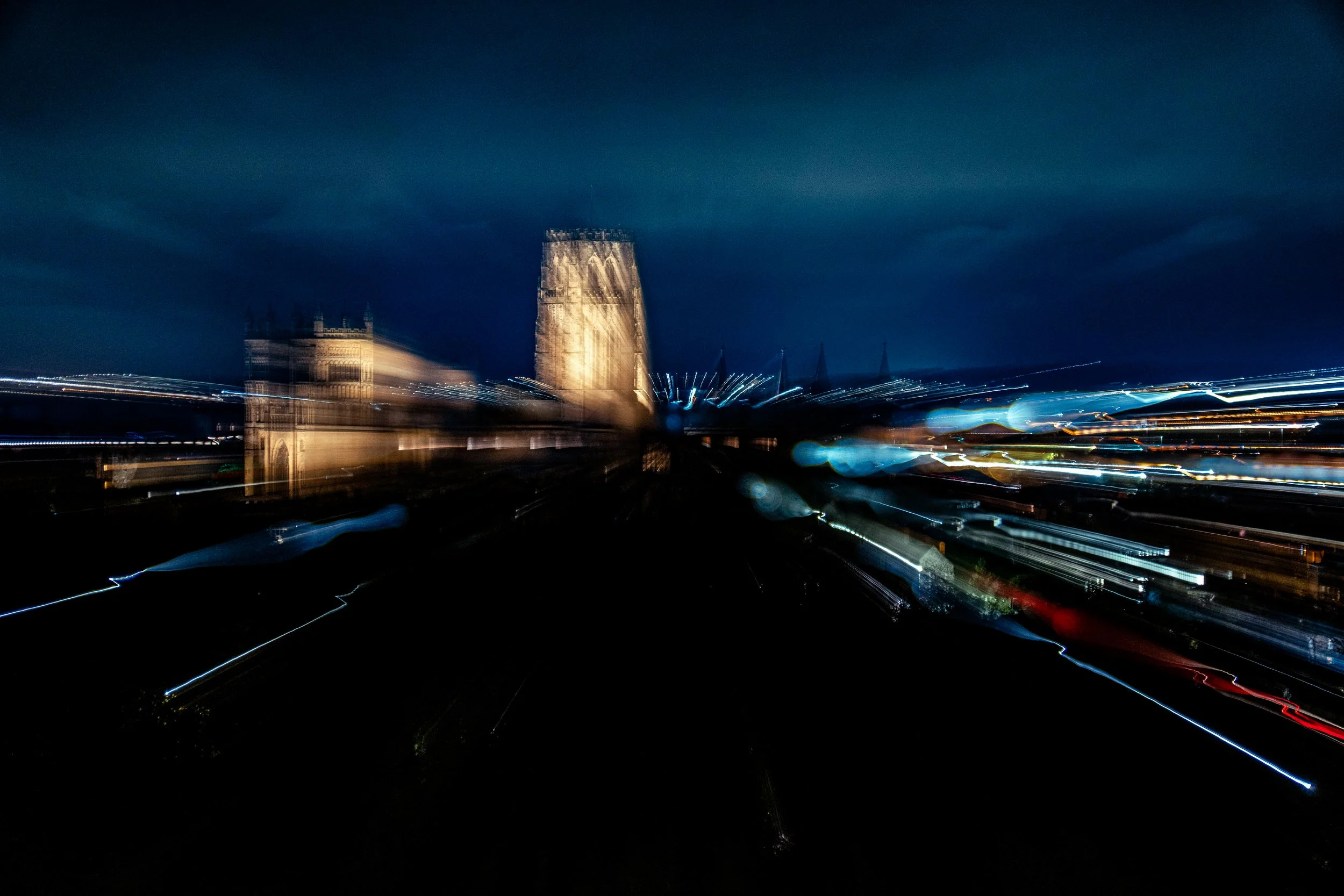 A long exposure night photo of Big Ben and the London skyline, with light trails from moving vehicles visible in the foreground.