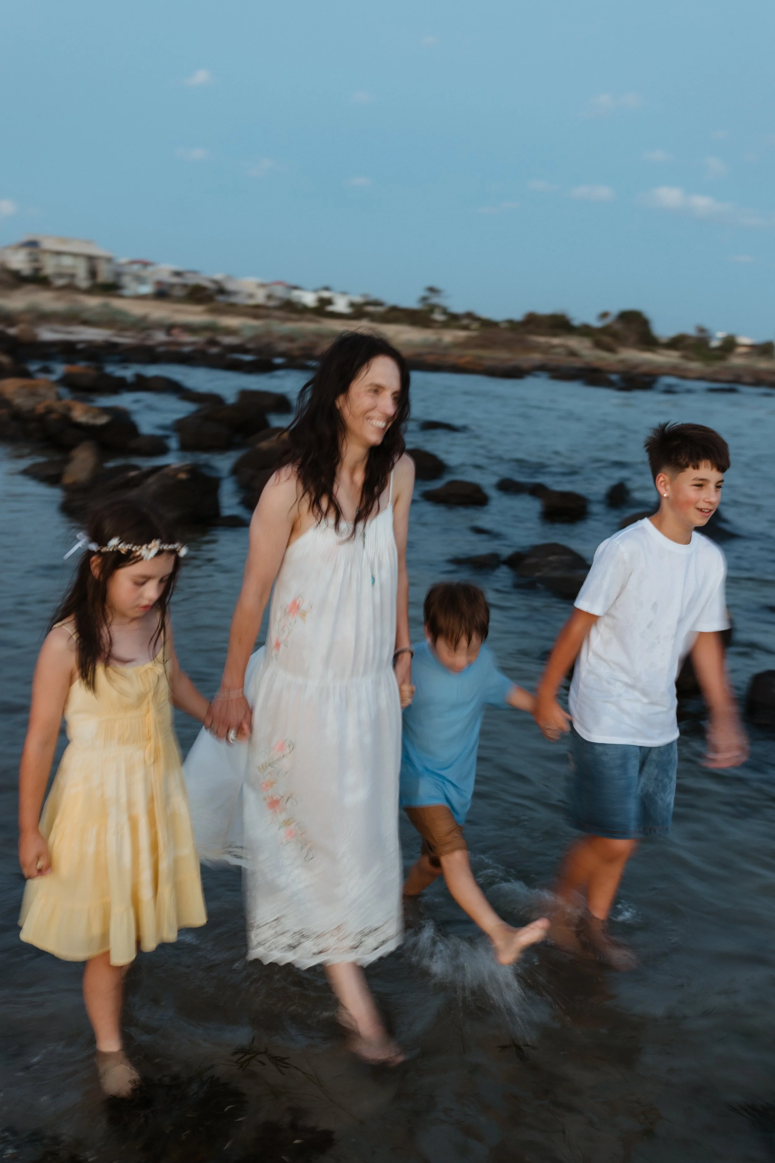 Jenna Chia walking hand in hand with her children through water at the beach — reflecting the warm, nurturing and holistic approach of Luminescence Kinesiology, Seddon Melbourne. Photo by Amy Oliver.