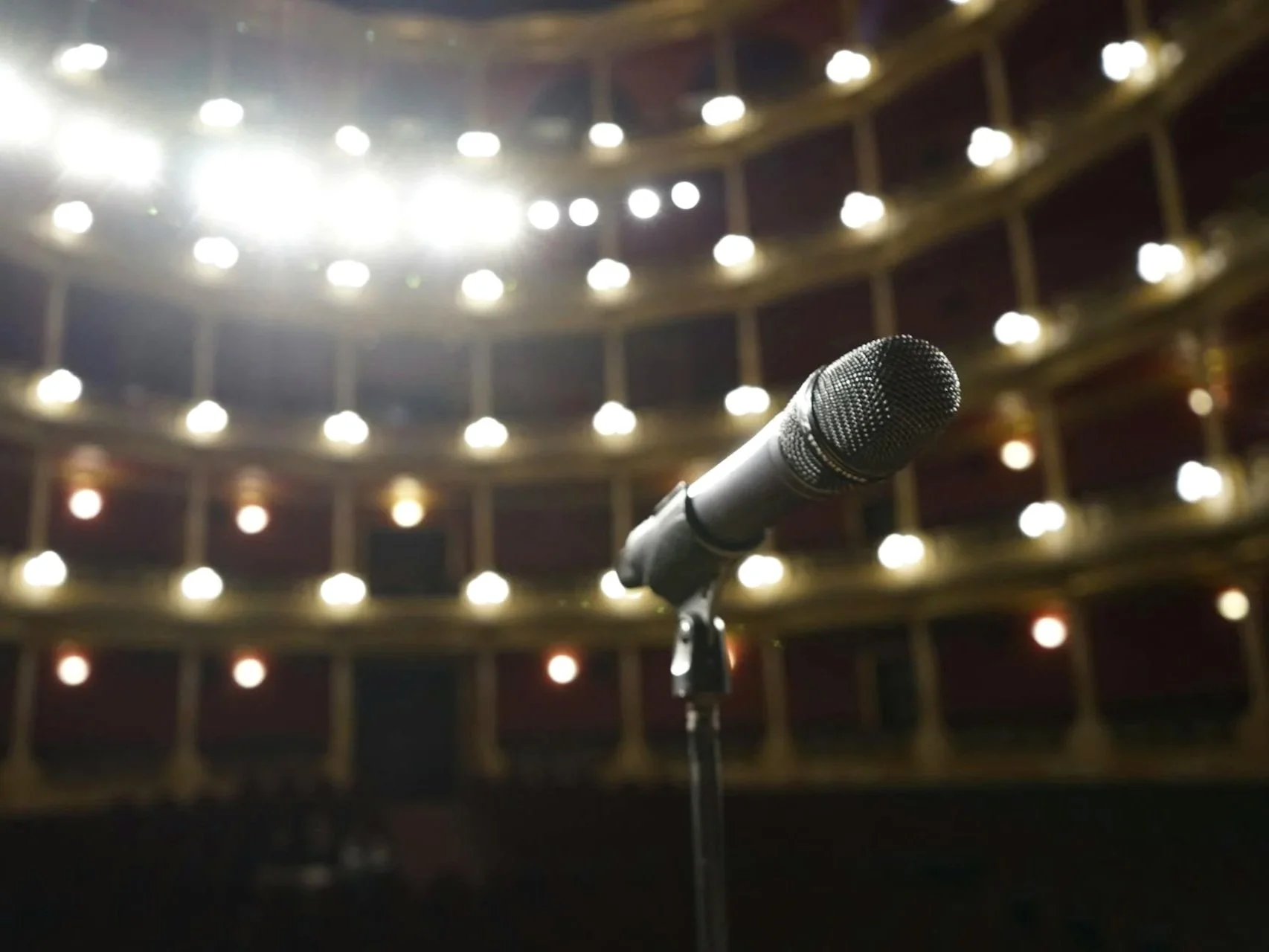 Microphone on stage in a theater with an audience seating area and bright stage lights overhead.