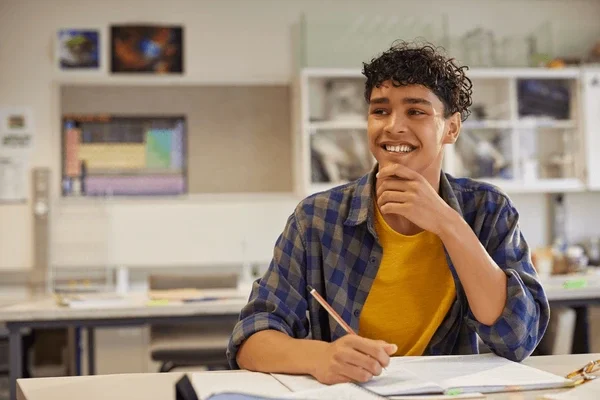 A student sitting at a desk in a classroom, smiling with books on the desk thinking about carnival or compound interest.
