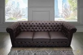 Brown tufted sofa in front of a window with a view of trees.