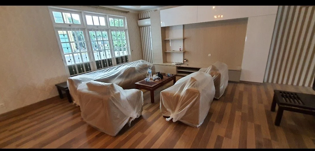 Living room with plastic-covered furniture, a wooden coffee table with water bottles and remote controls, large windows, and striped wallpaper.