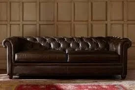 A dark brown leather tufted sofa in a room with wooden paneled walls and a red area rug.