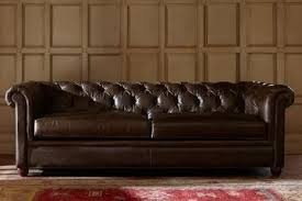 A dark brown leather tufted sofa in front of a beige paneled wall.