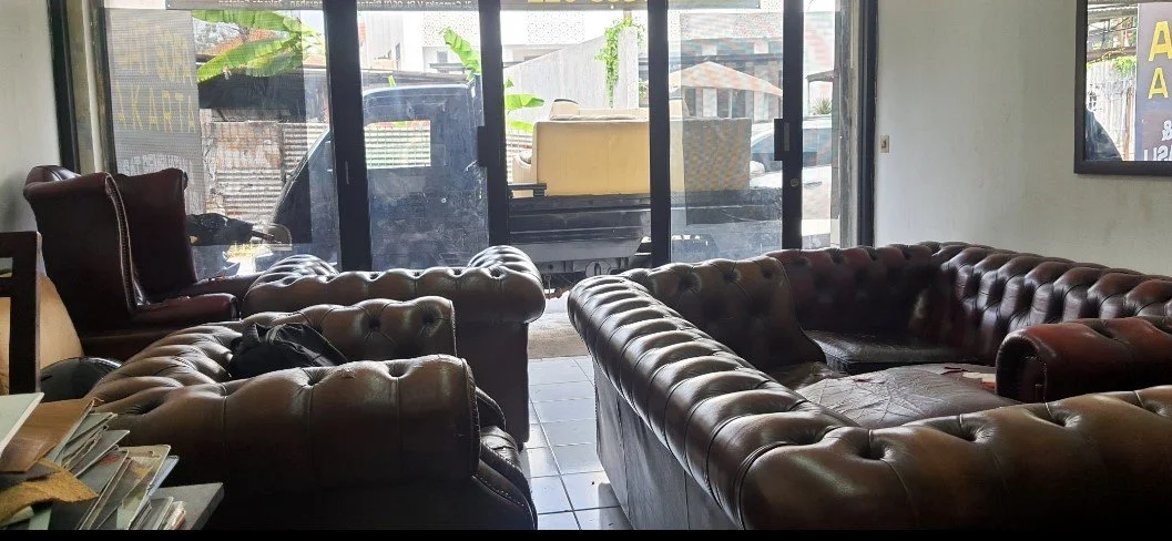 Interior of a coffee shop or lounge with large leather sofas, cluttered with books and personal items, near glass doors leading outside.