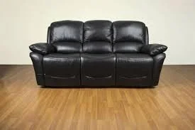 Black leather sofa on wooden floor against a plain wall.