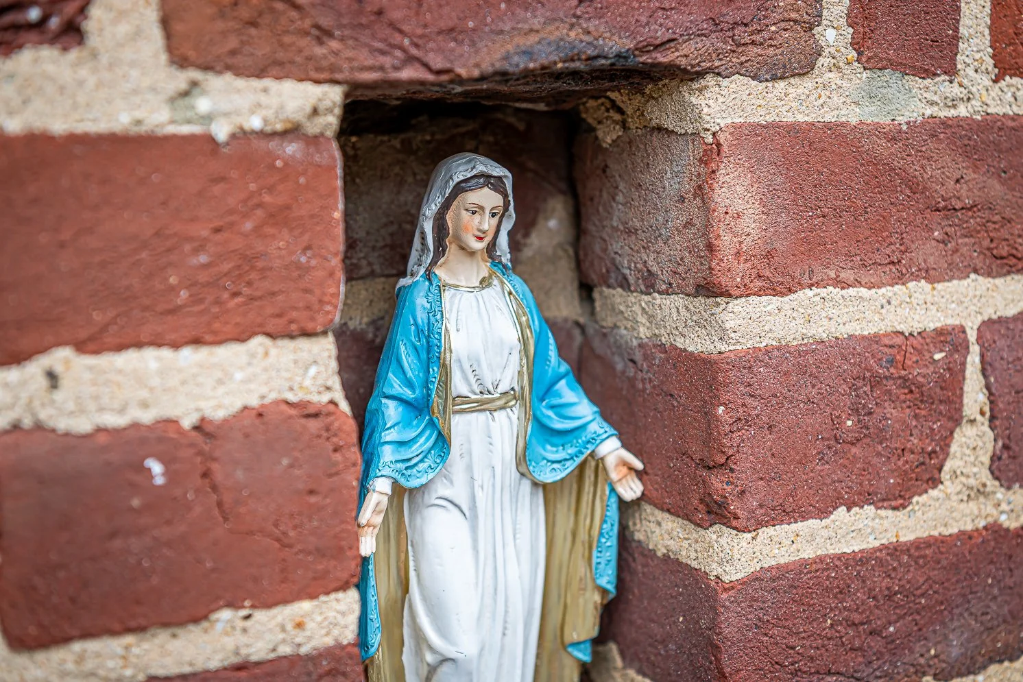 Een beeld van de Maagd Maria die in een nis in een bakstenen muur staat