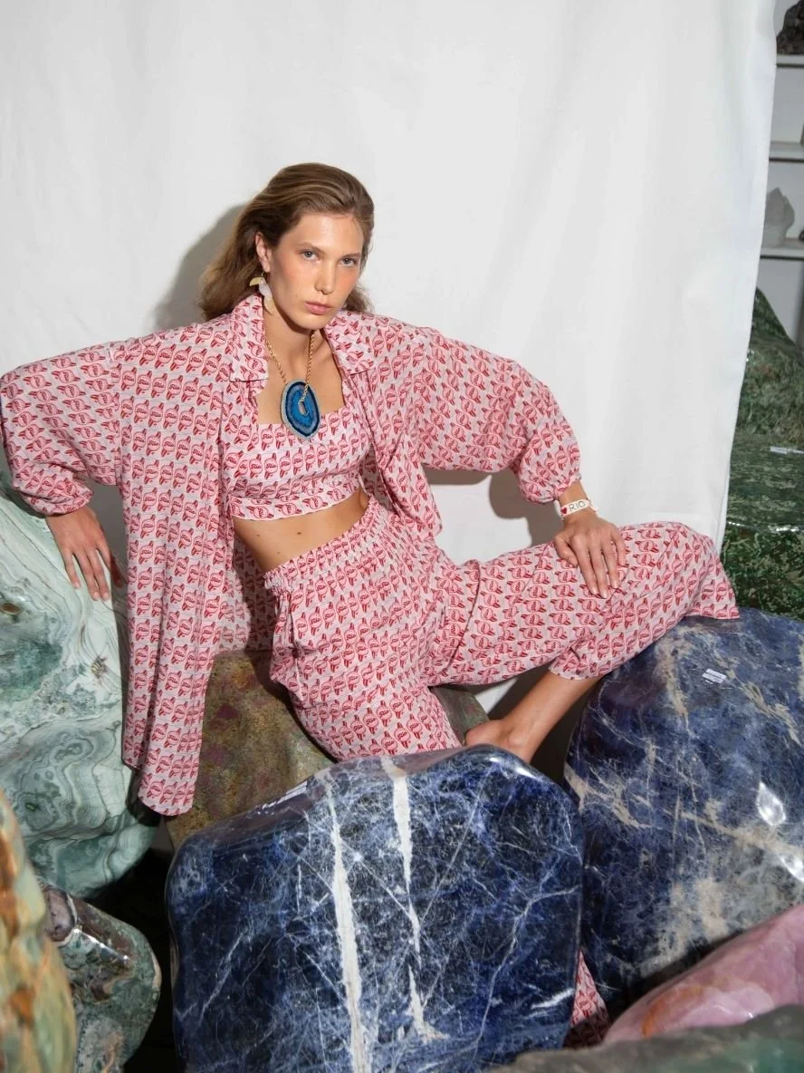 A woman in a pink patterned outfit seated on colorful rocks with a white backdrop behind her.