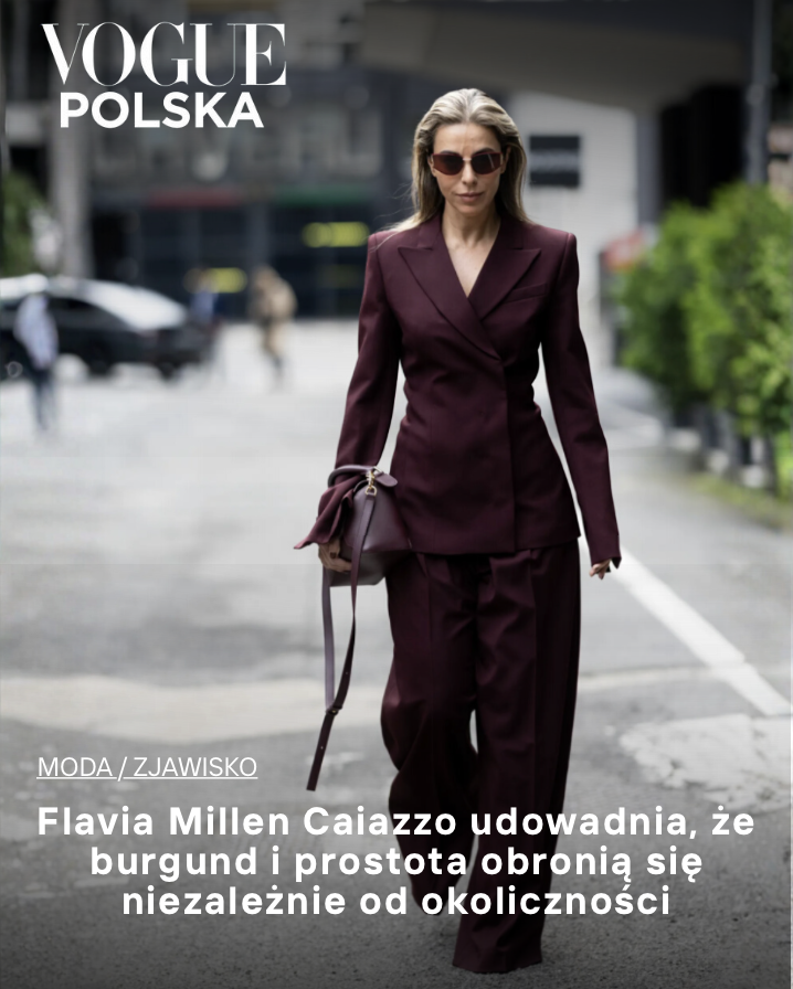 A woman in a burgundy suit walking outdoors on a city street, wearing sunglasses and carrying a matching handbag. Vogue POSKA
