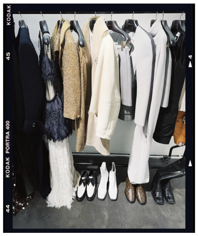 Clothing rack with various jackets, coats, and dresses, along with two pairs of white boots and two pairs of black and brown boots underneath.