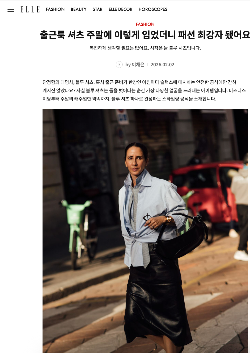 A woman walking on a city street, dressed in a light blue shirt and black leather skirt, carrying a black purse, with a red car and a green bicycle in the background.