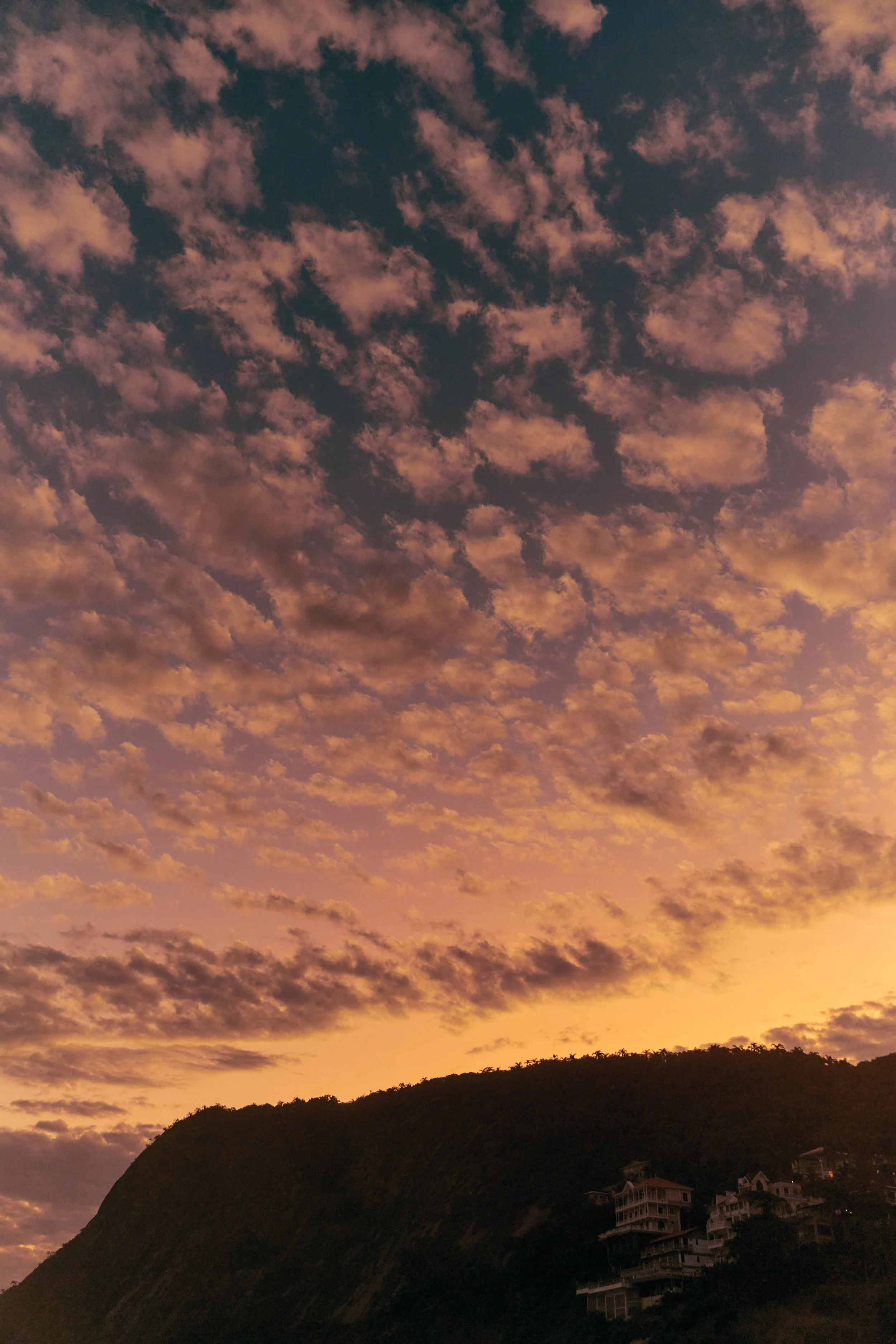 Sunset sky with pink and orange clouds over a hillside with residential houses.