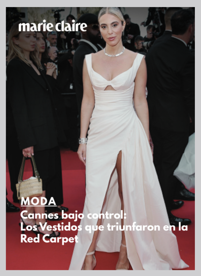 A woman wearing an elegant white dress with a high slit, standing on a red carpet at the Cannes Film Festival, surrounded by other attendees and photographers.