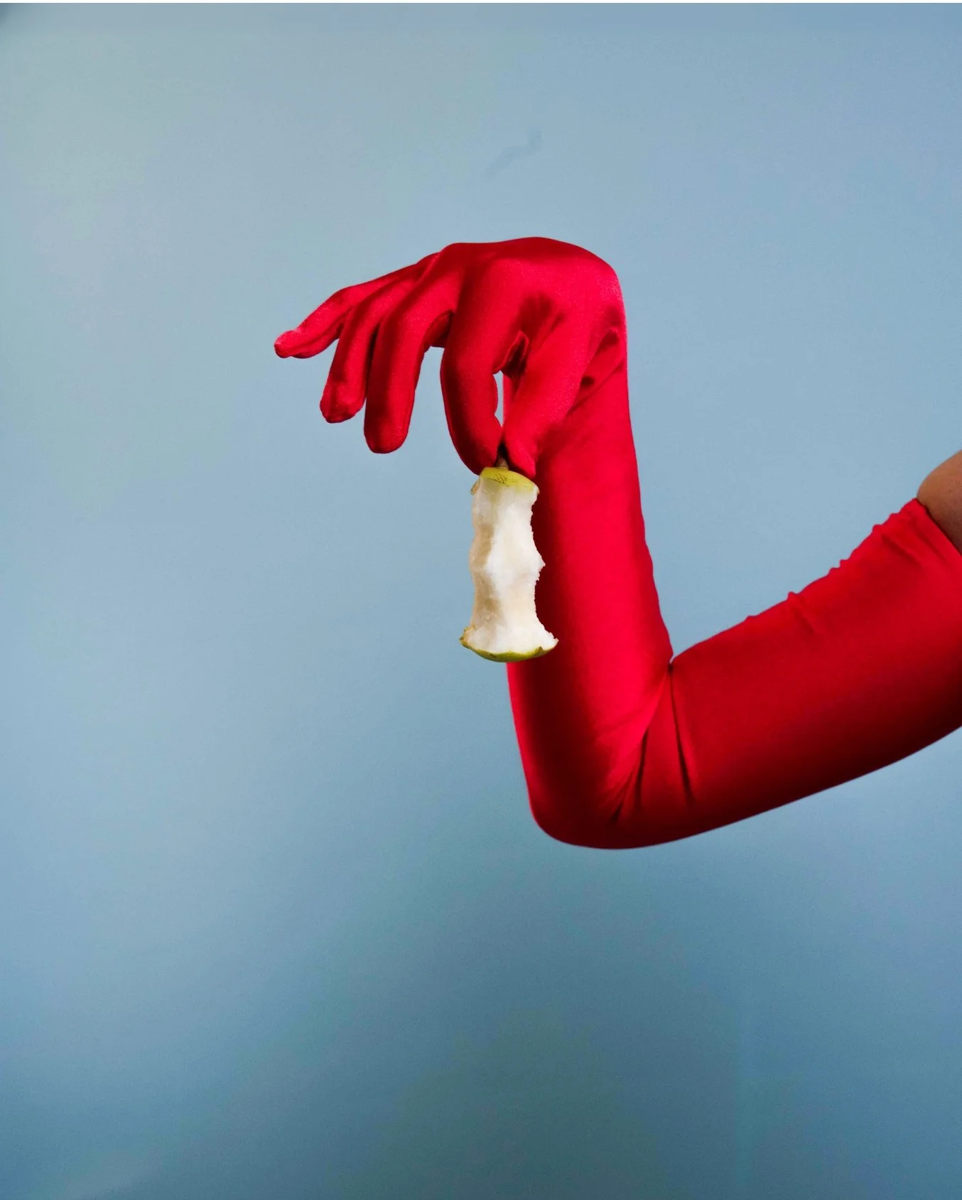 A person wearing a red long-sleeved shirt and red gloves is holding a partially eaten apple against a plain gray background.