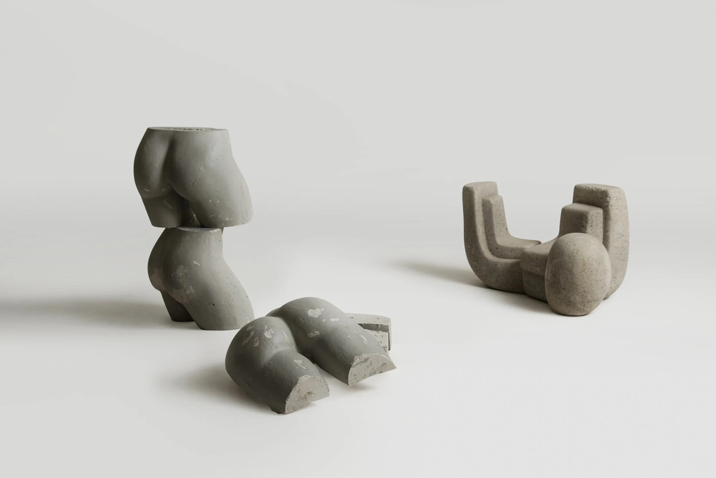 Two abstract sculpture figures made of stone or concrete with a minimalist design, set against a plain white background.