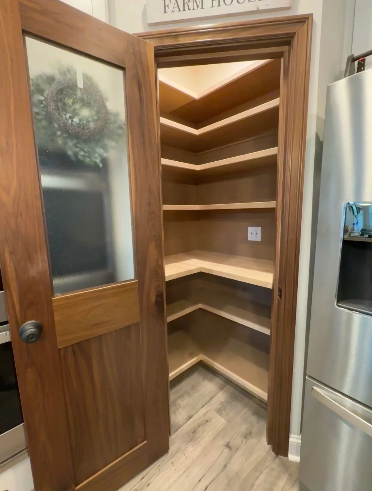 Empty corner pantry with wooden shelves in a kitchen, with a wooden door featuring frosted glass.