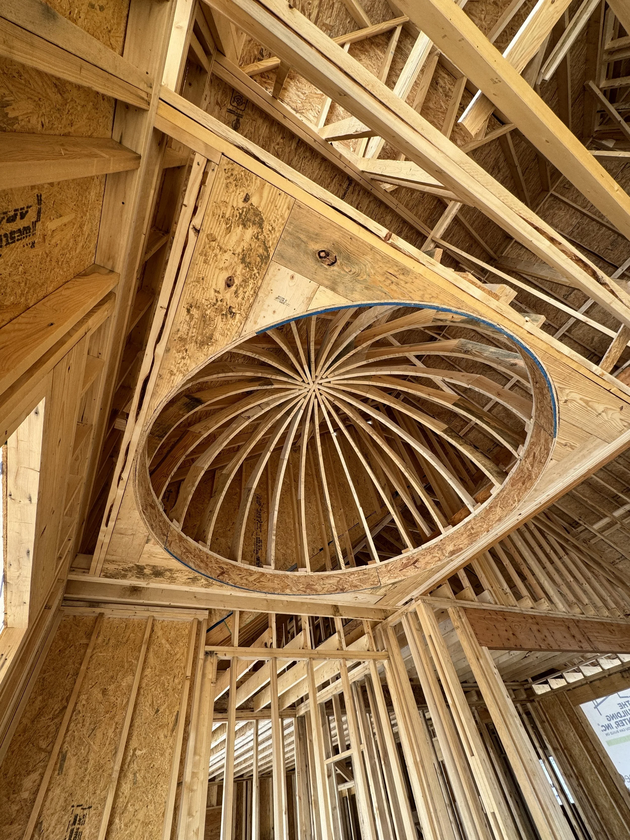 The interior framing of a building under construction, with wooden studs, floor sheathing, and a circular opening in the ceiling structure.