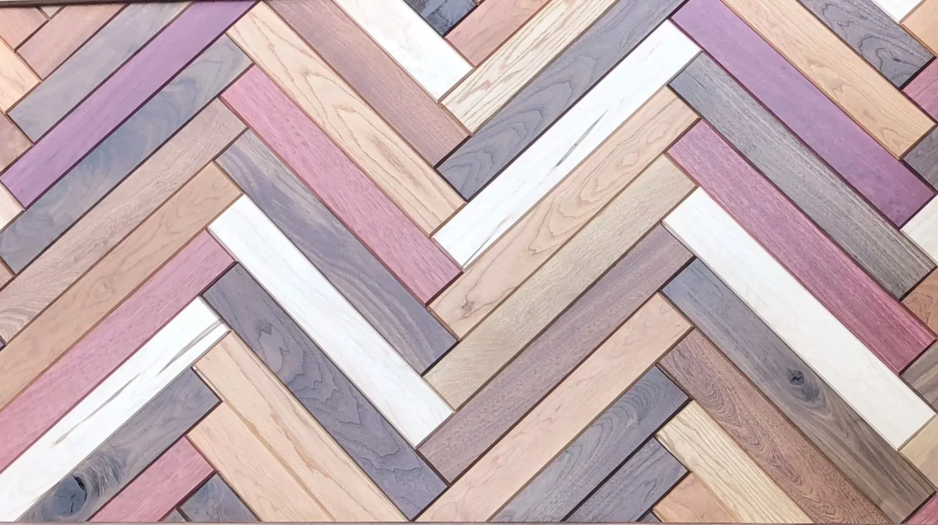 Colorful wooden parquet flooring arranged in a herringbone pattern with various shades of pink, gray, white, and natural wood tones.
