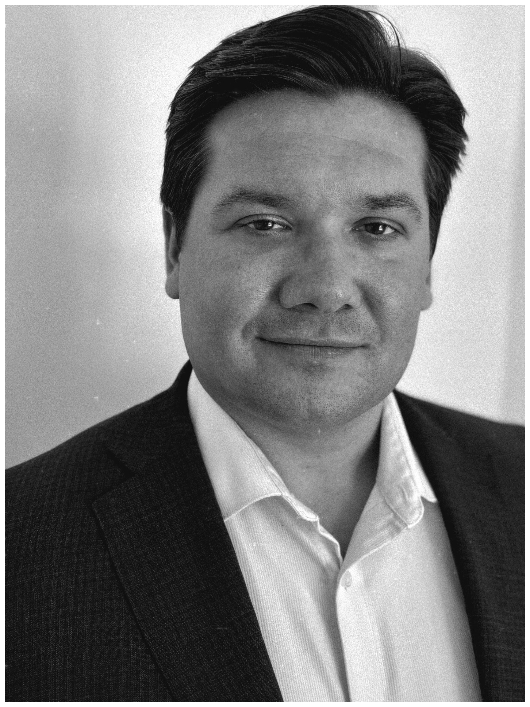 Black and white professional headshot of a man wearing a dark suit and white shirt, smiling slightly, with neatly combed hair.