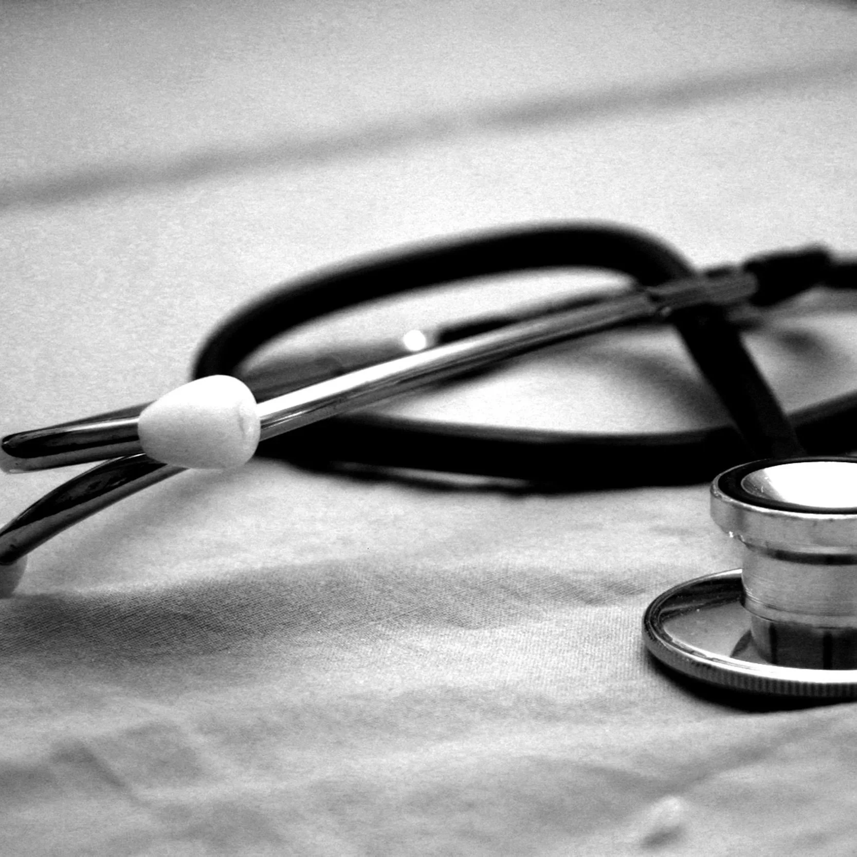 Close-up black-and-white photo of medical tools, including a stethoscope and a tuning fork, on a flat surface.