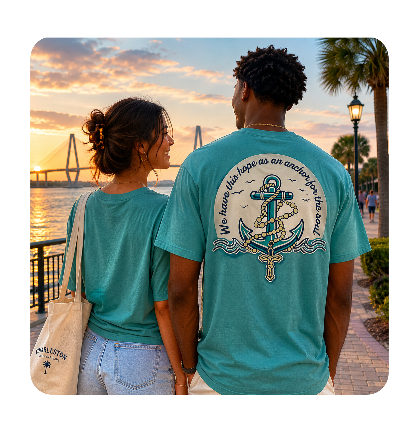 A young couple holding hands and looking at each other while walking along a waterfront during sunset, with the man wearing a turquoise T-shirt with an anchor and rope design on the back, and the woman holding a tote bag with Charleston, South Carolina written on it.