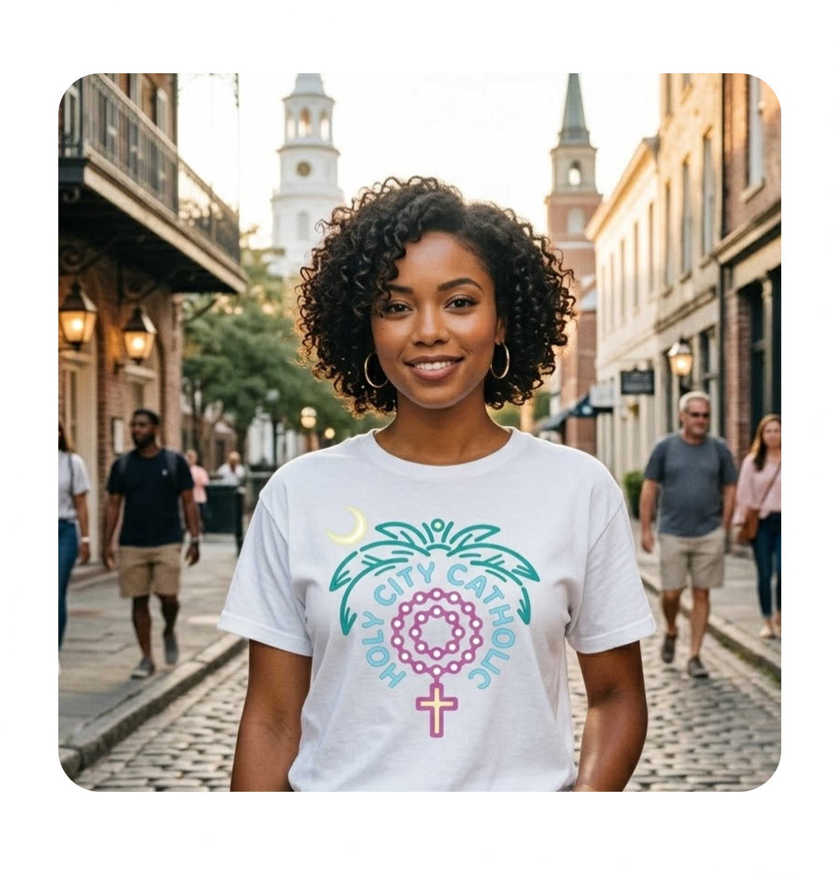 A young woman with curly hair smiling and standing on a cobblestone street with historic buildings and church steeples in the background. She is wearing a white t-shirt with a feminist graphic and text.