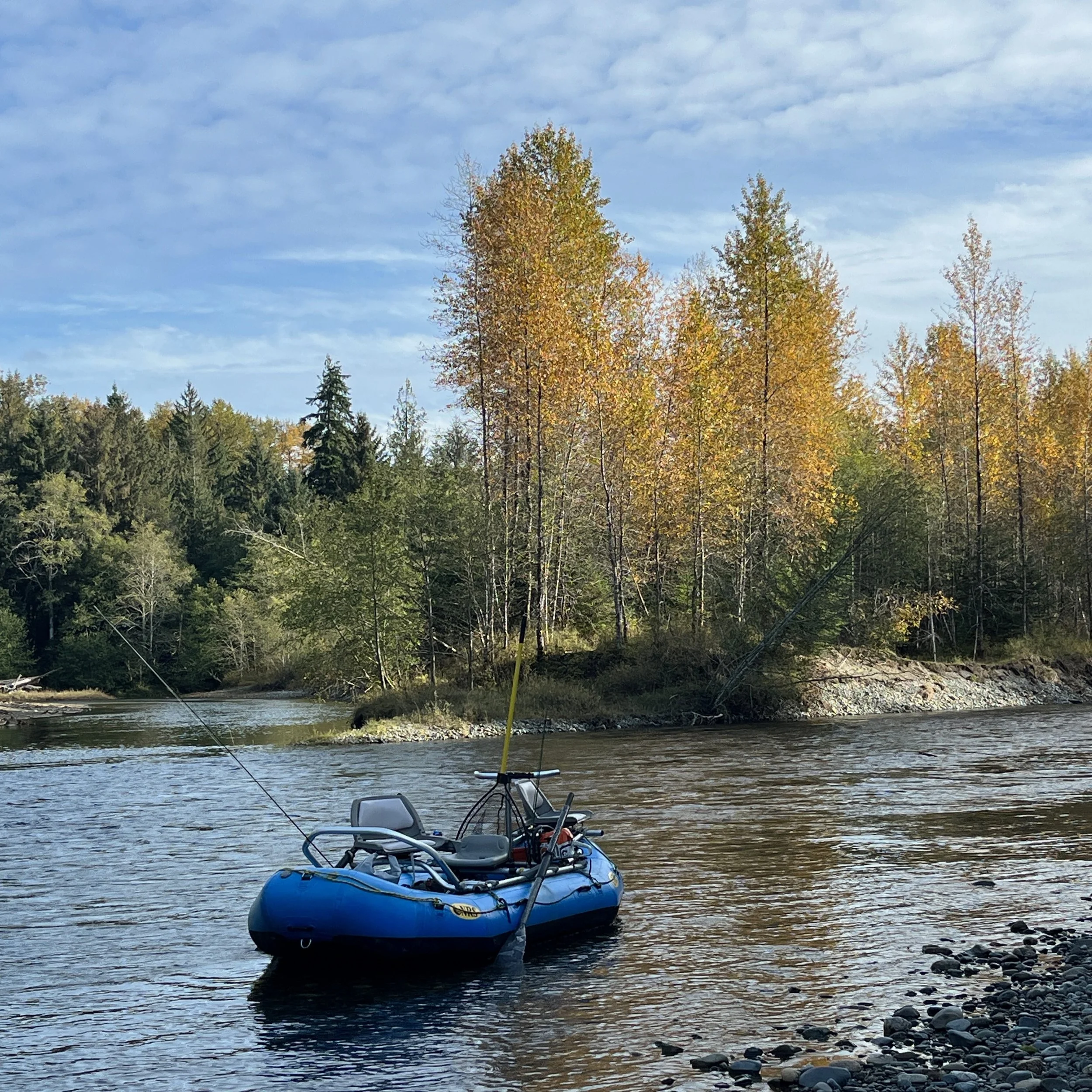 A river scene with a fishing boat, trees with autumn foliage, and a partly cloudy sky.