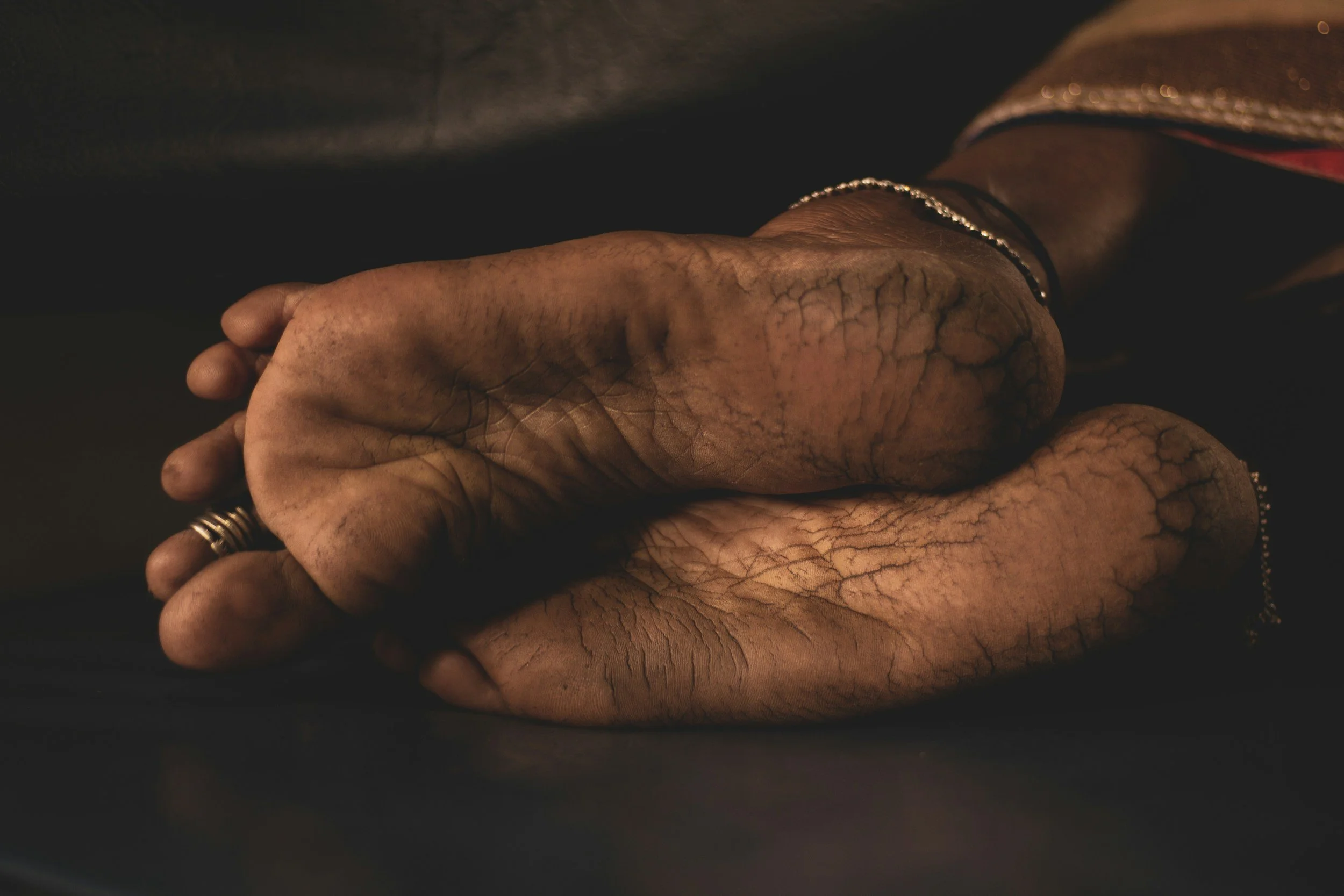 Close-up of two people holding hands, one with darker skin and tattoos, wearing jewelry, against a dark background.