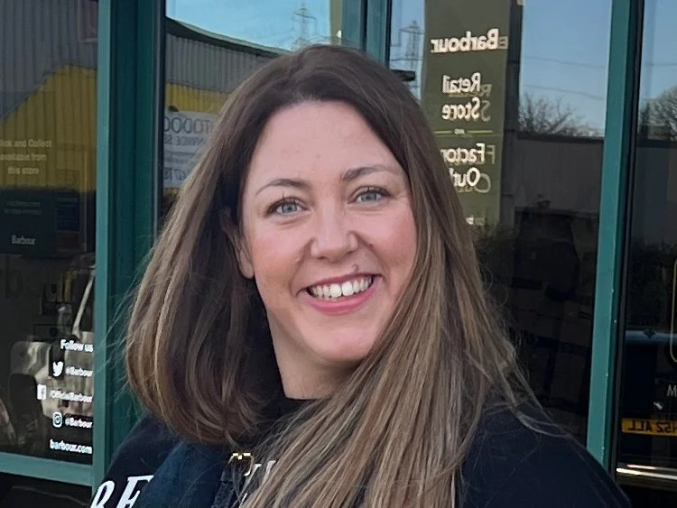 A woman with long brown hair smiling outside a storefront with green framing.