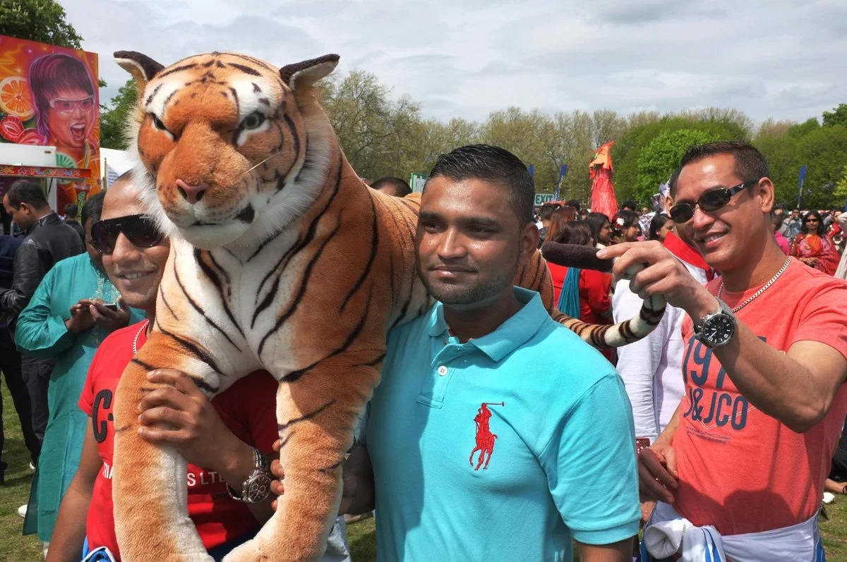 Group of people outdoors with a man holding a large tiger mascot costume, surrounded by smiling individuals in casual clothing.