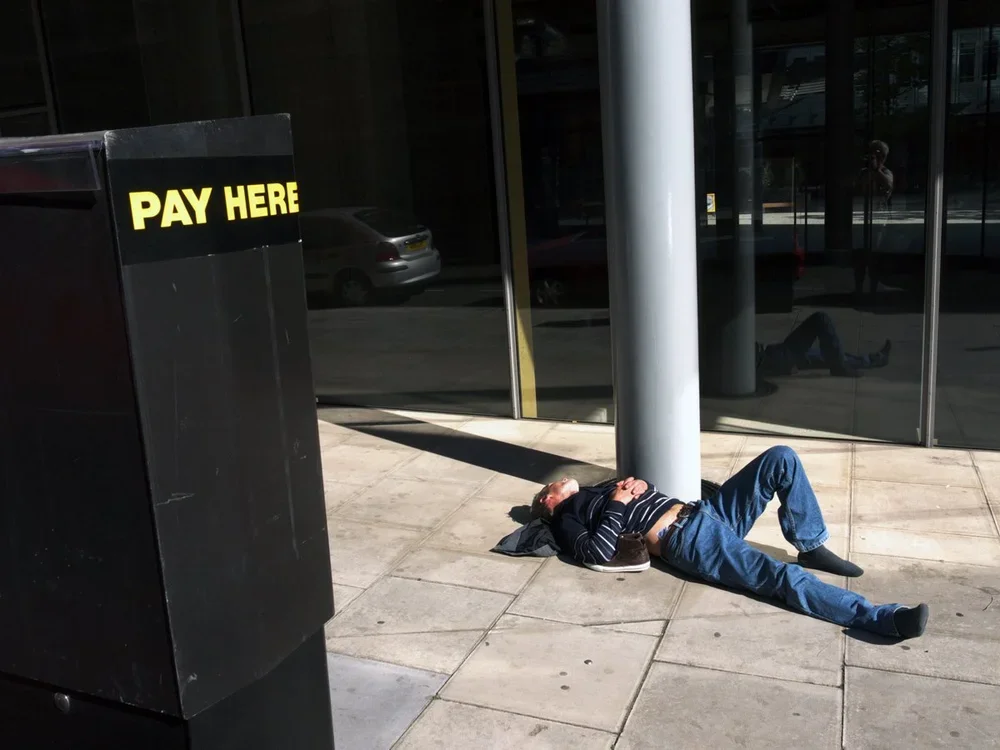 Person lying on the sidewalk next to a large black 