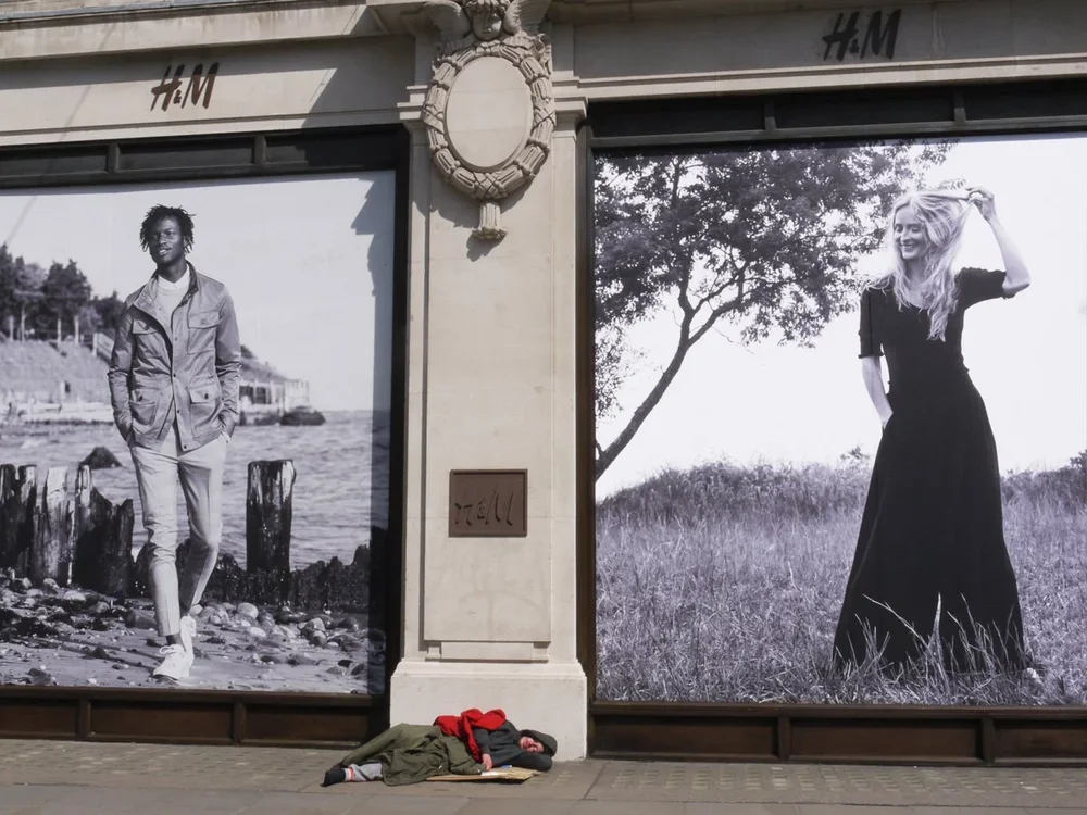 Two large black and white photographs of a man and a woman displayed on a building storefront, with a person sleeping on the sidewalk below.