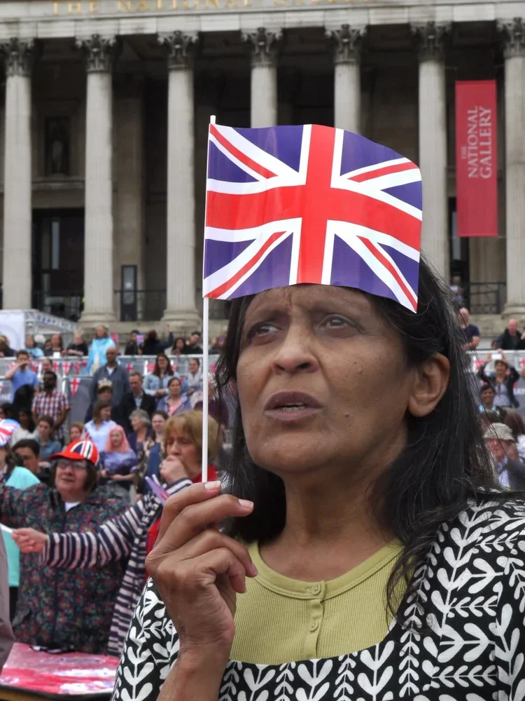 A woman holding a Union Jack flag at a gathering in front of a historic building with columns and a banner that reads "National Gallery."
